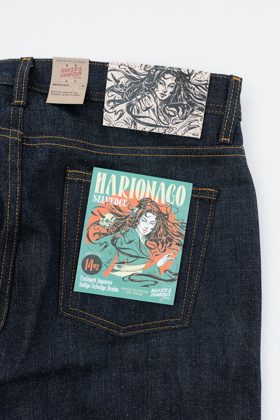 Close-up back view of dark indigo selvedge denim jeans with yellow stitching, showing back pocket, waistband tags, and Marionago artwork.