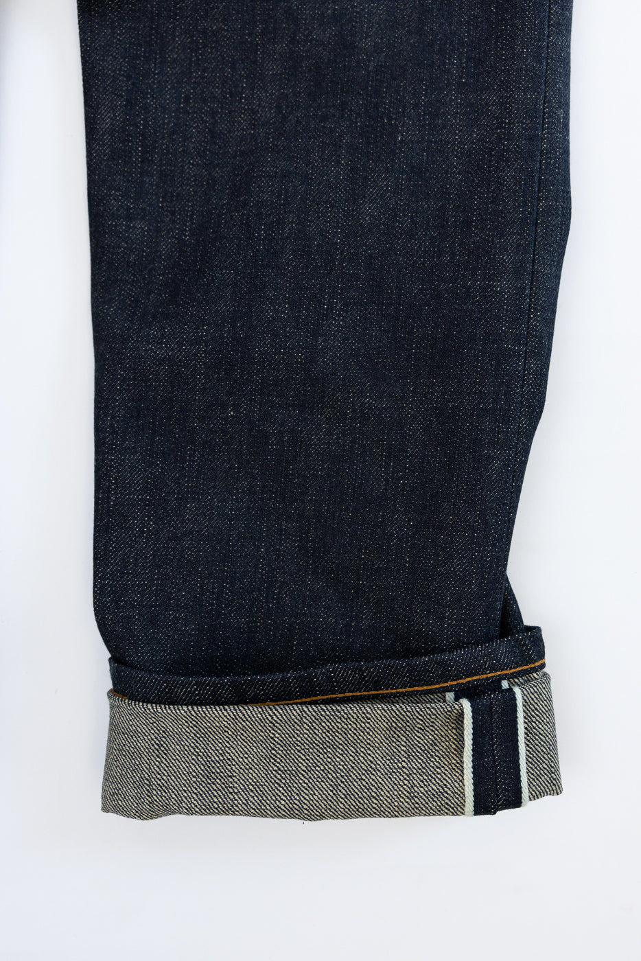 Close-up of dark selvedge denim jeans cuff, showcasing fabric texture and contrast stitching