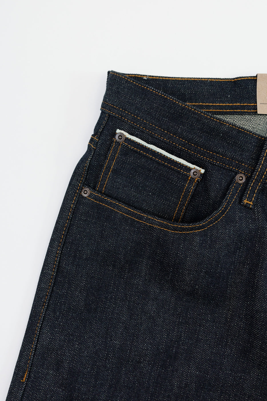 Close-up front view of dark selvedge denim jeans with orange stitching and button details