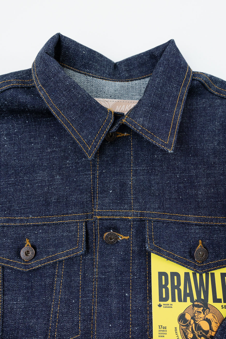 Close-up front view of dark denim jacket with pointed collar, copper buttons, yellow stitching, and selvedge tag detail