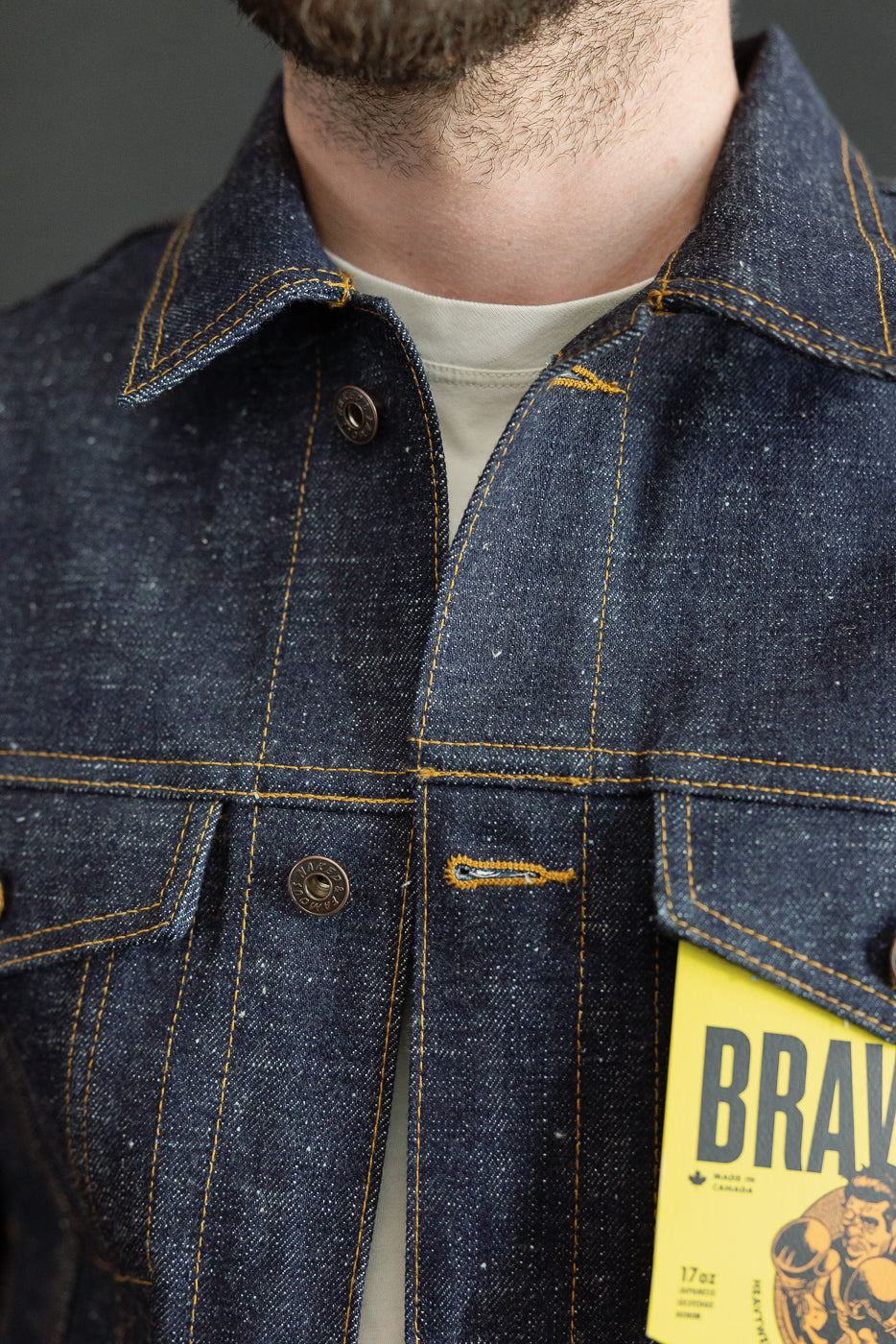Close-up front view of male model wearing raw denim jacket with yellow stitching, button closure, and chest pockets