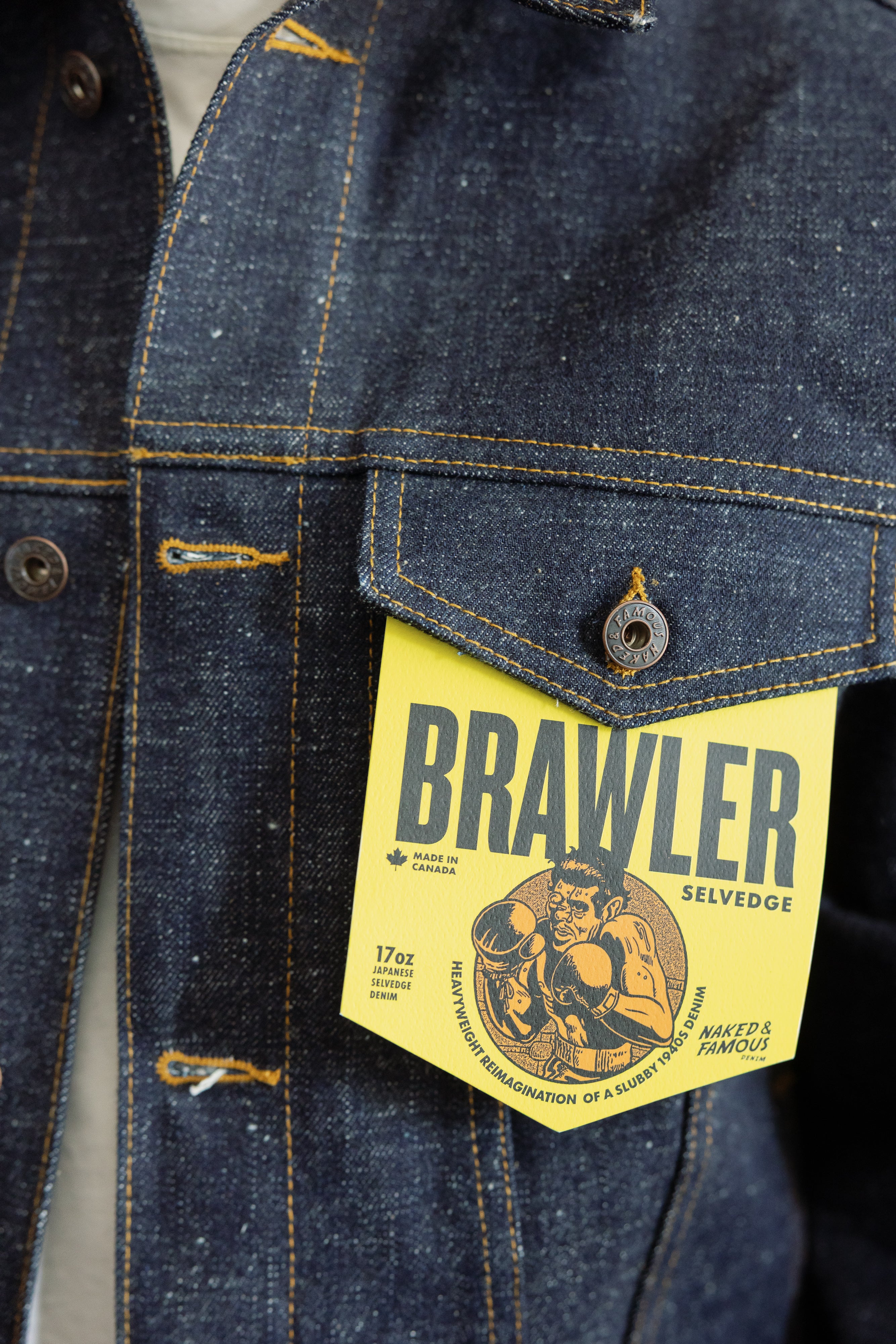 Close-up front of men's 17oz Japanese selvedge denim jacket, showing chest pocket, yellow stitching, and Brawler tag.