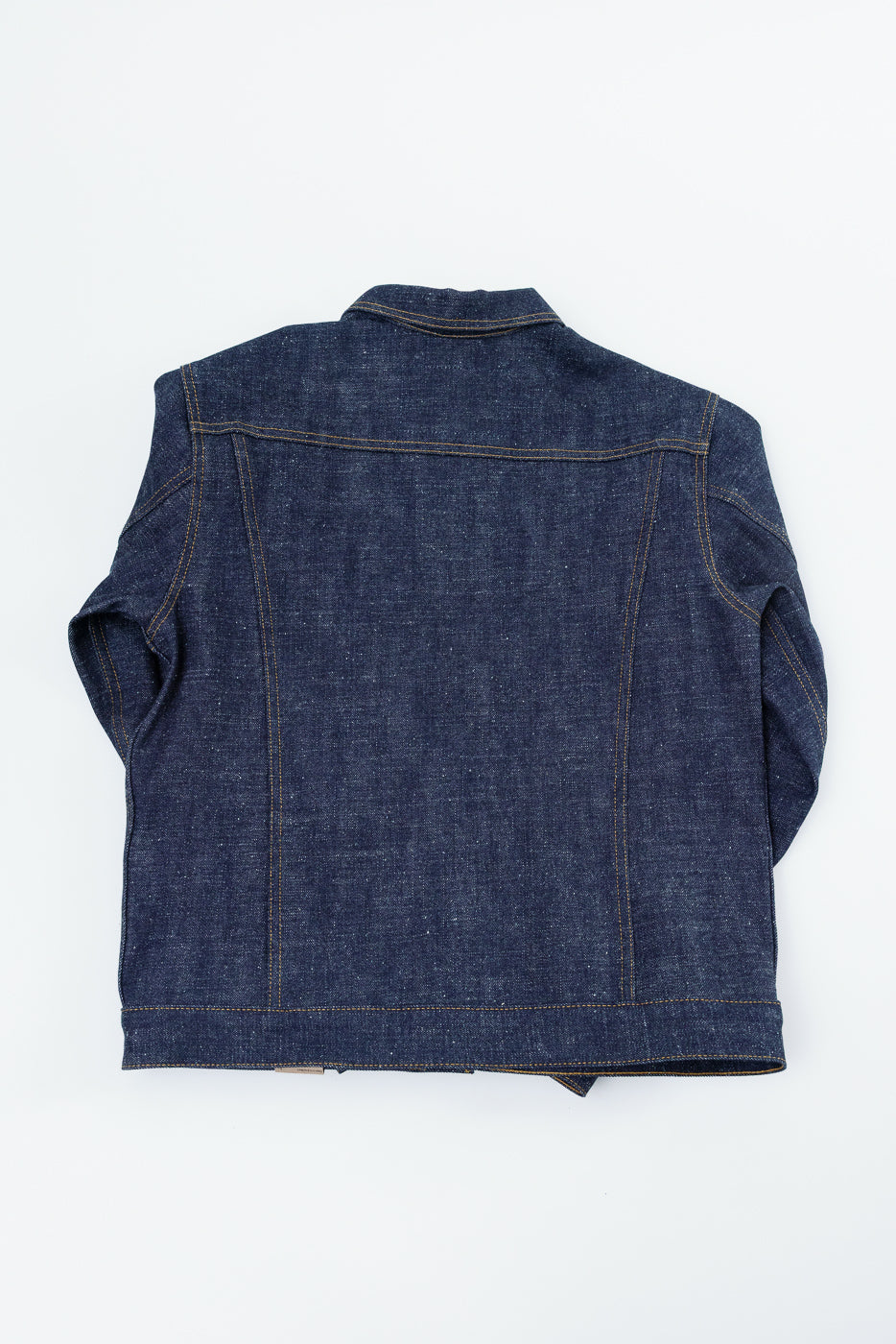 Back view of raw selvedge denim jacket, flat lay, showing yoke stitching and hem detail