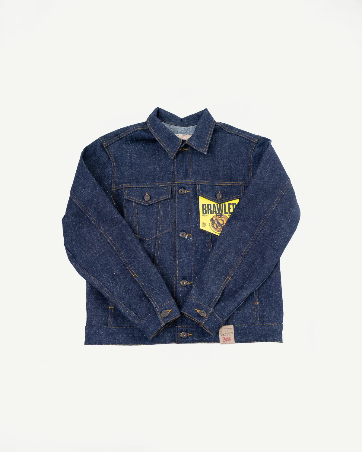 Front flat lay of men's raw denim jacket with button closure, chest pockets, yellow BRAWLER tag, and selvedge details