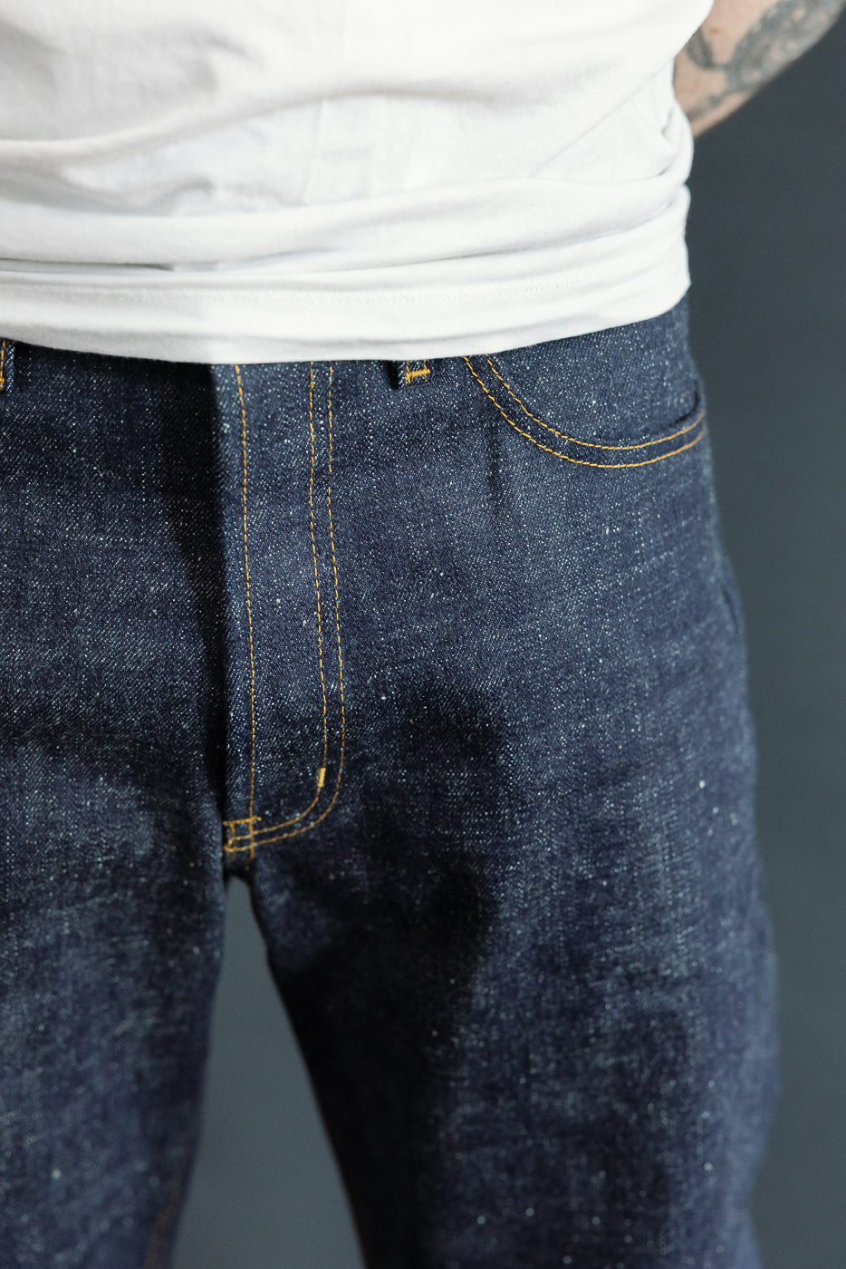 Close-up front view of dark selvedge denim jeans with gold stitching, worn by male model, 5'9