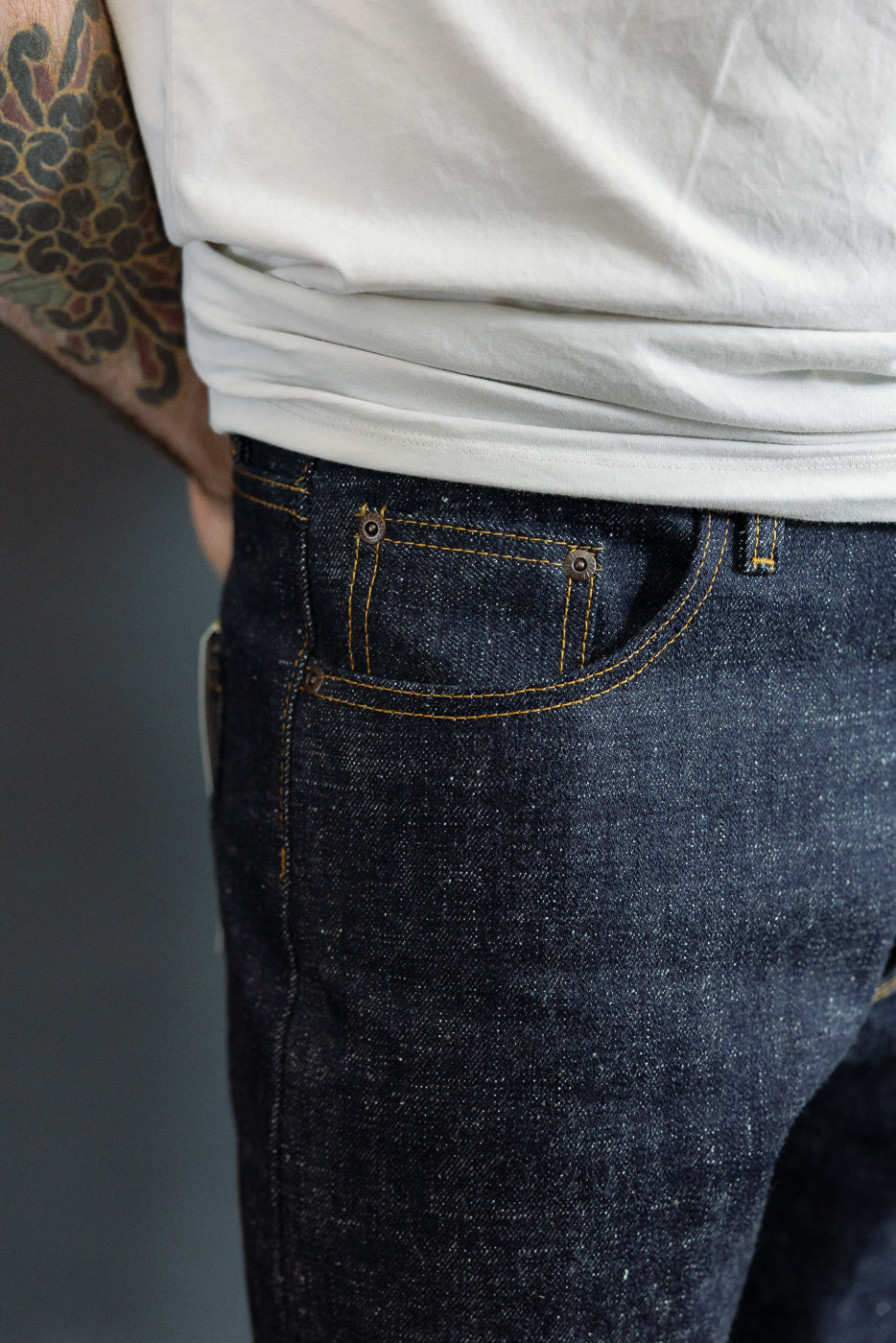 Close-up front view of dark selvedge denim jeans with yellow stitching, worn by male model, 5'9