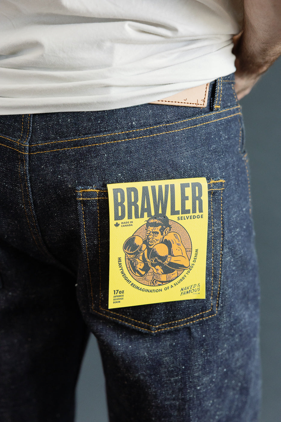 Close-up back view of male model wearing dark selvedge denim jeans with yellow 'Brawler' patch, 17oz Japanese denim, tan stitching