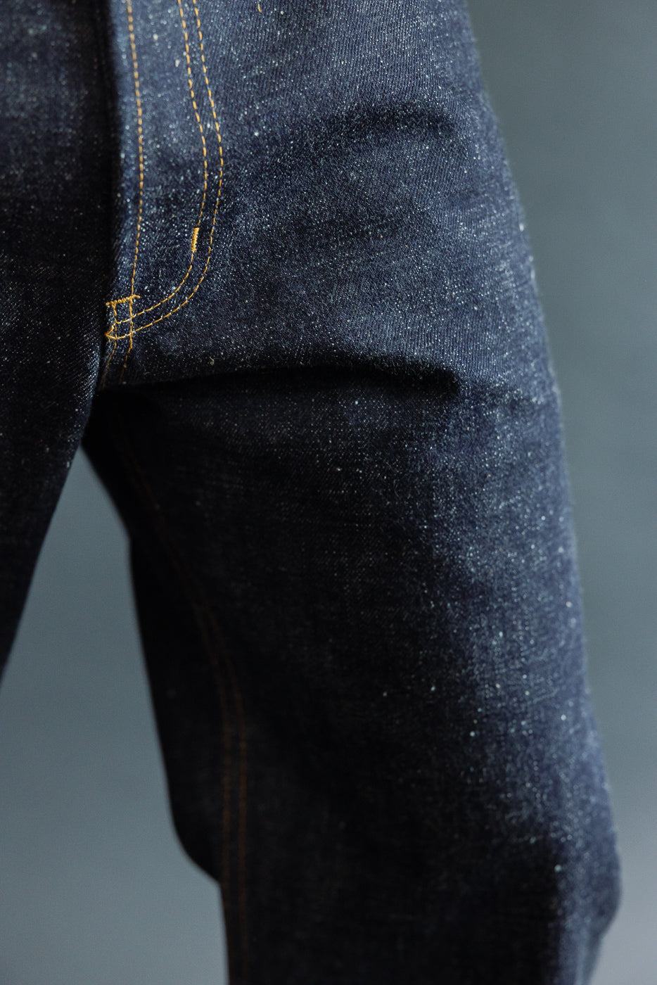 Close-up of selvedge denim jeans showing back pocket with gold stitching, worn by male model.