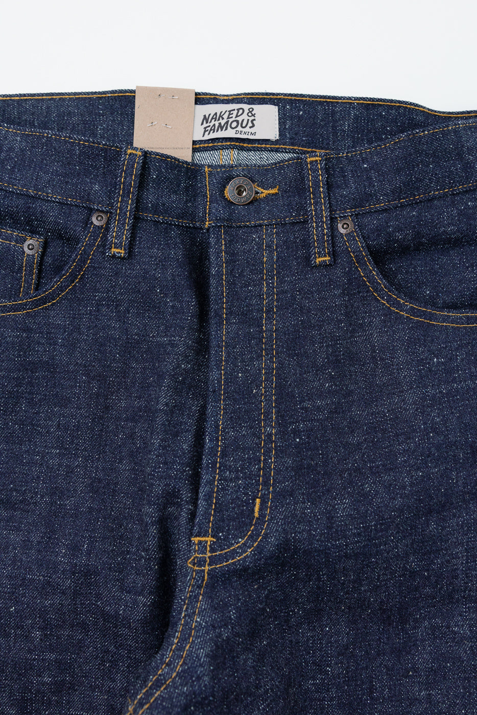 Close-up front view of dark selvedge denim jeans with yellow stitching, button fly, and Naked & Famous tag.