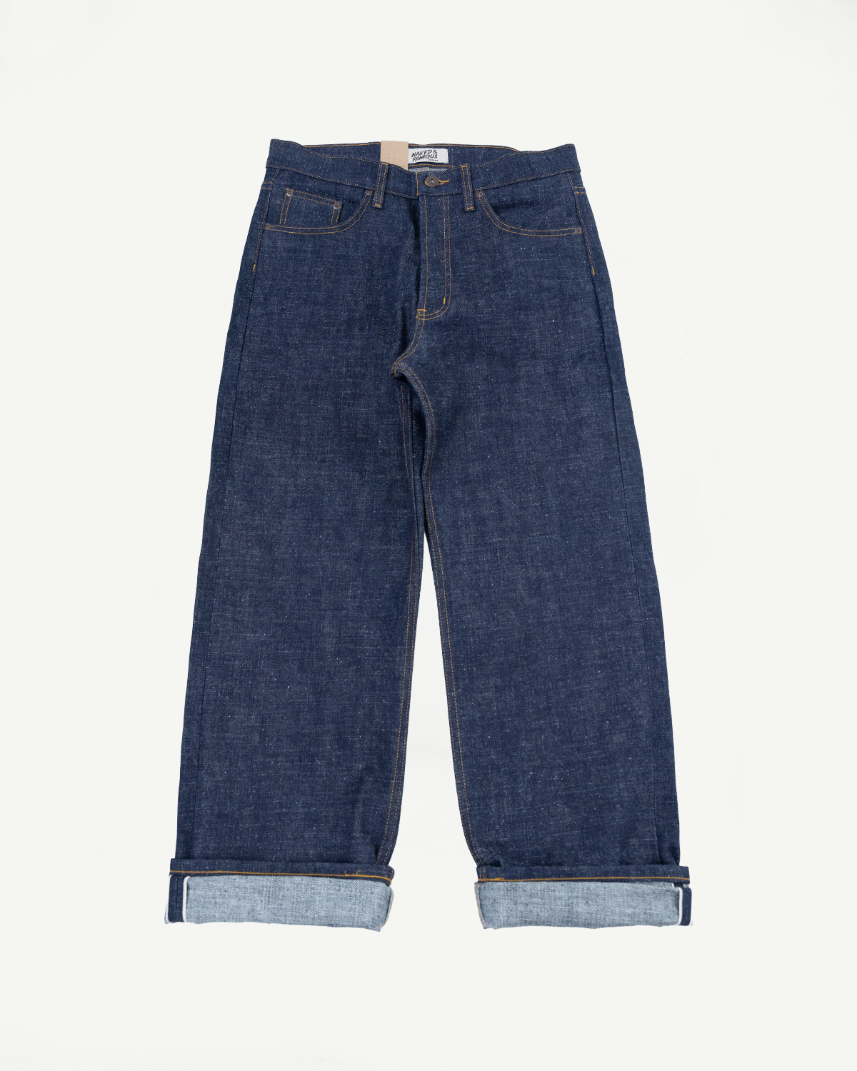 Front flat lay of raw selvedge denim jeans with cuffed hems, yellow stitching, and brand tag visible