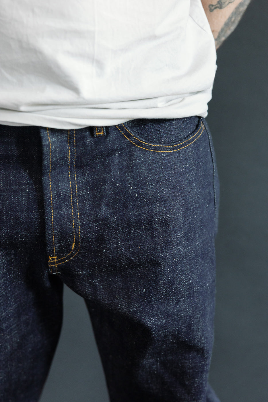 Close-up front view of male model's dark selvedge jeans with yellow stitching, athletic build