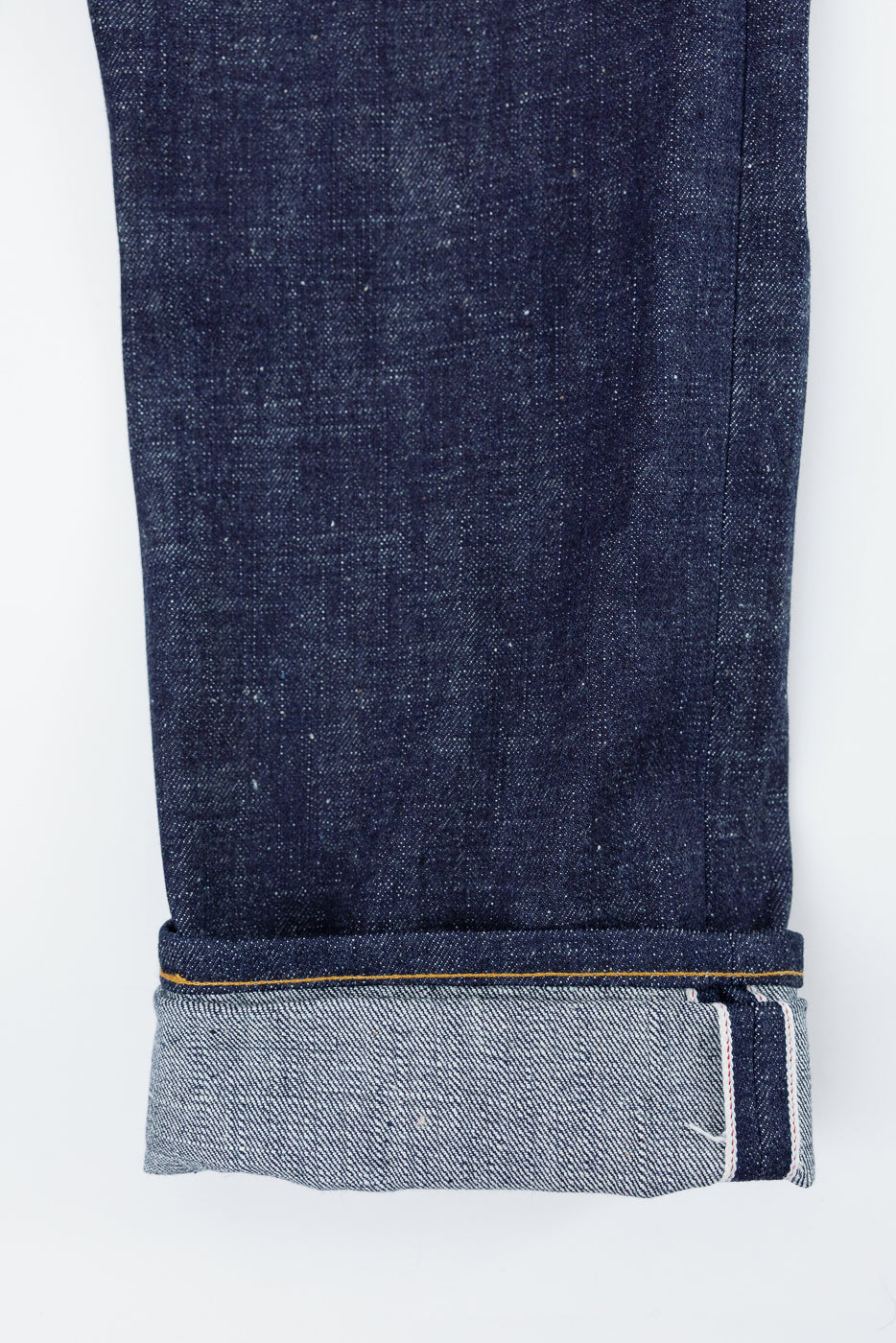 Close-up front view of selvedge denim jeans leg, showing raw hem, contrast stitching, and fabric texture