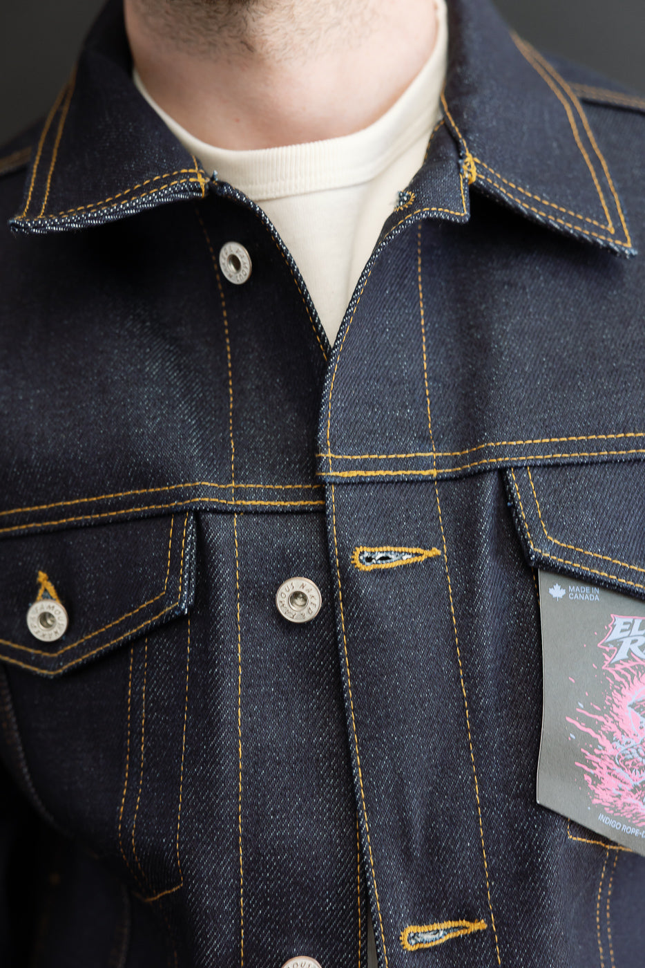 Close-up front view of dark indigo denim jacket showing collar, button details, and stitching.