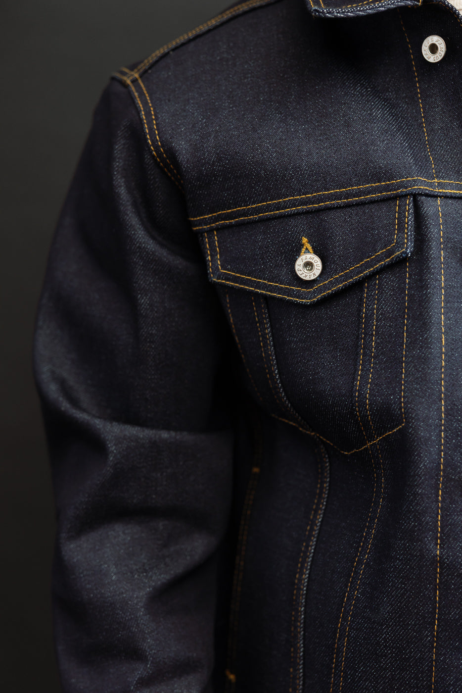 Close-up of the front chest and pocket area of a dark indigo selvedge denim jacket showing button detail.