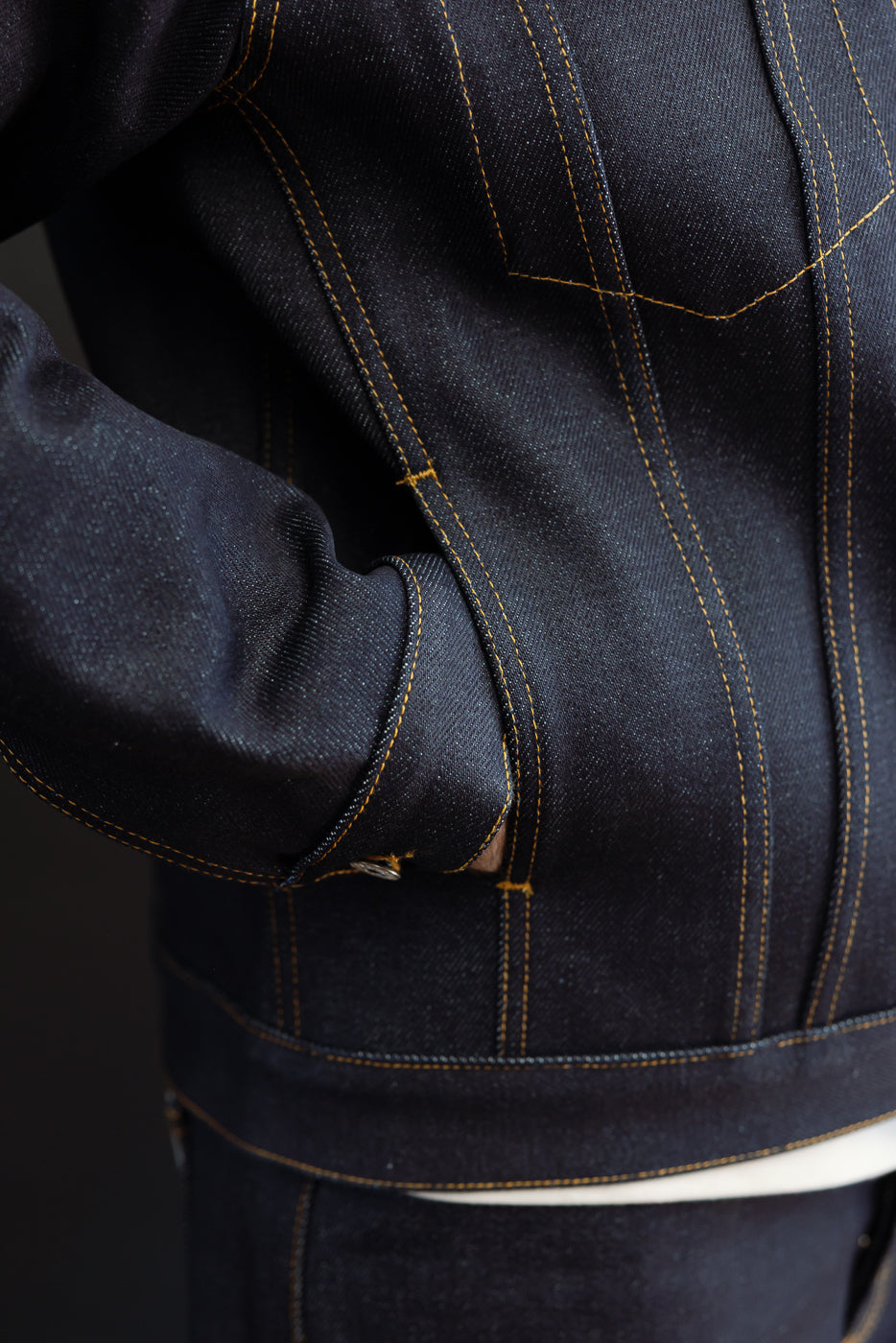 Close-up view of the back of a dark indigo selvedge denim jacket showing fabric texture and stitching.