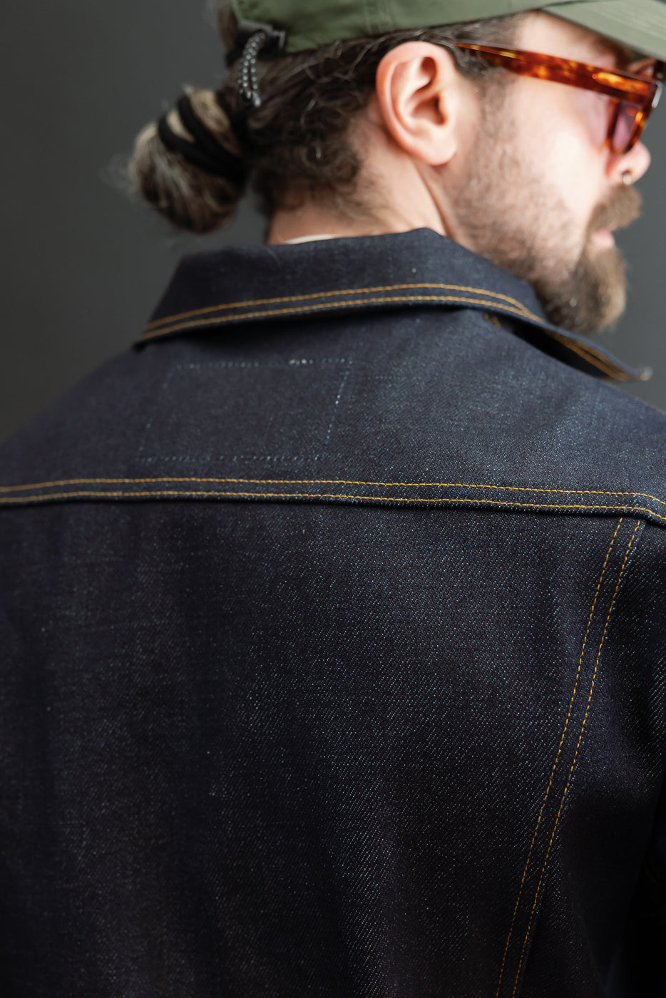 Close-up back view of a dark indigo denim jacket on a male model (5'9