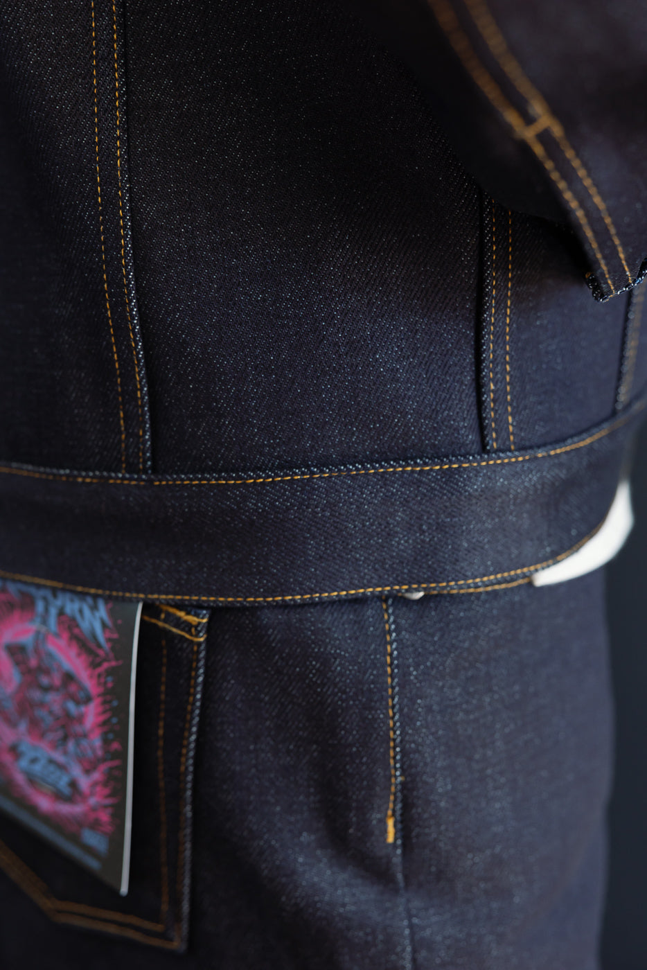 Close-up of the side of dark selvedge denim overalls with contrast stitching and pocket detail.