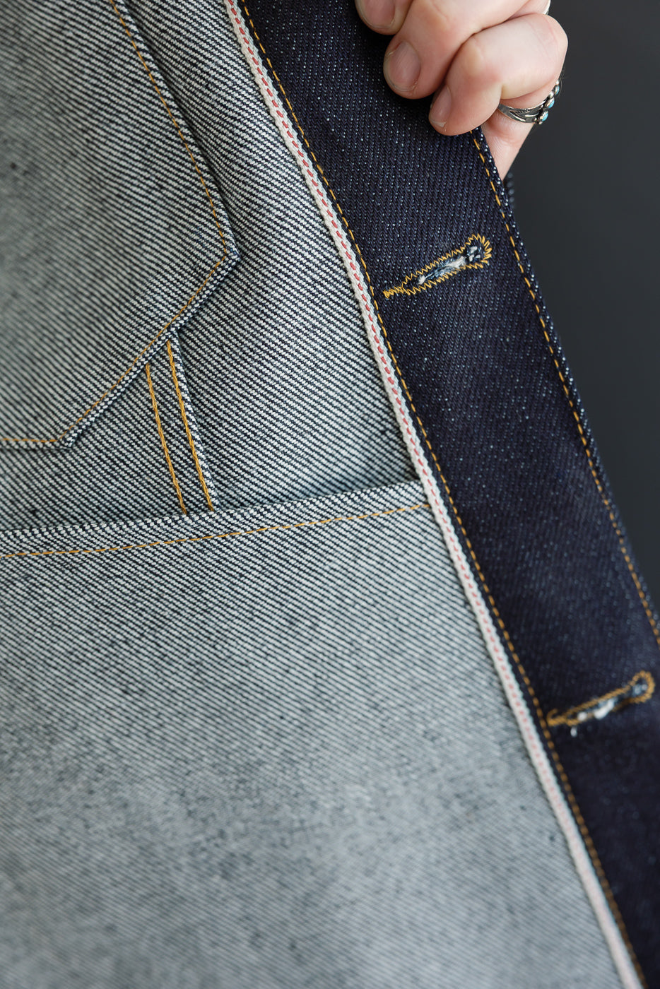 Close-up of a male model's left hip showing selvedge denim detail and orange stitching.