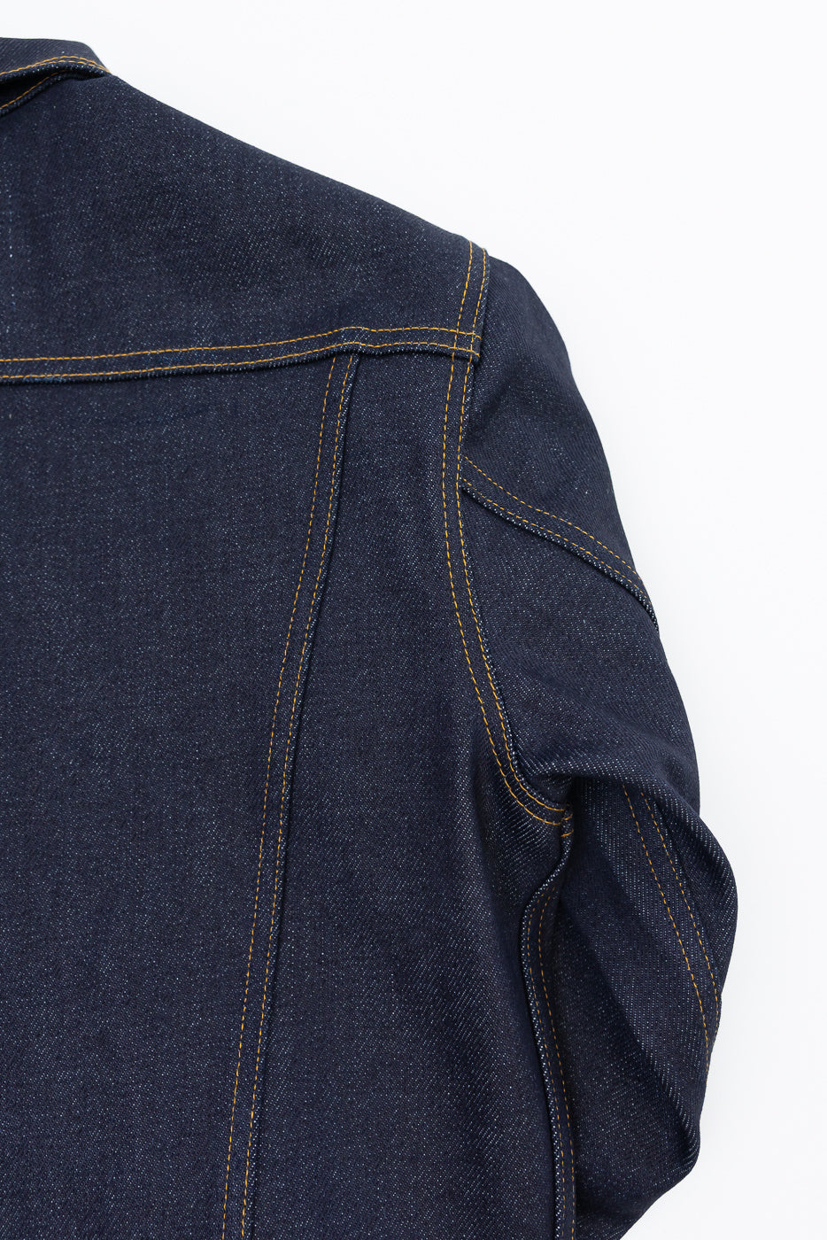 Close-up of the back shoulder and sleeve of a dark indigo denim jacket with gold stitching.