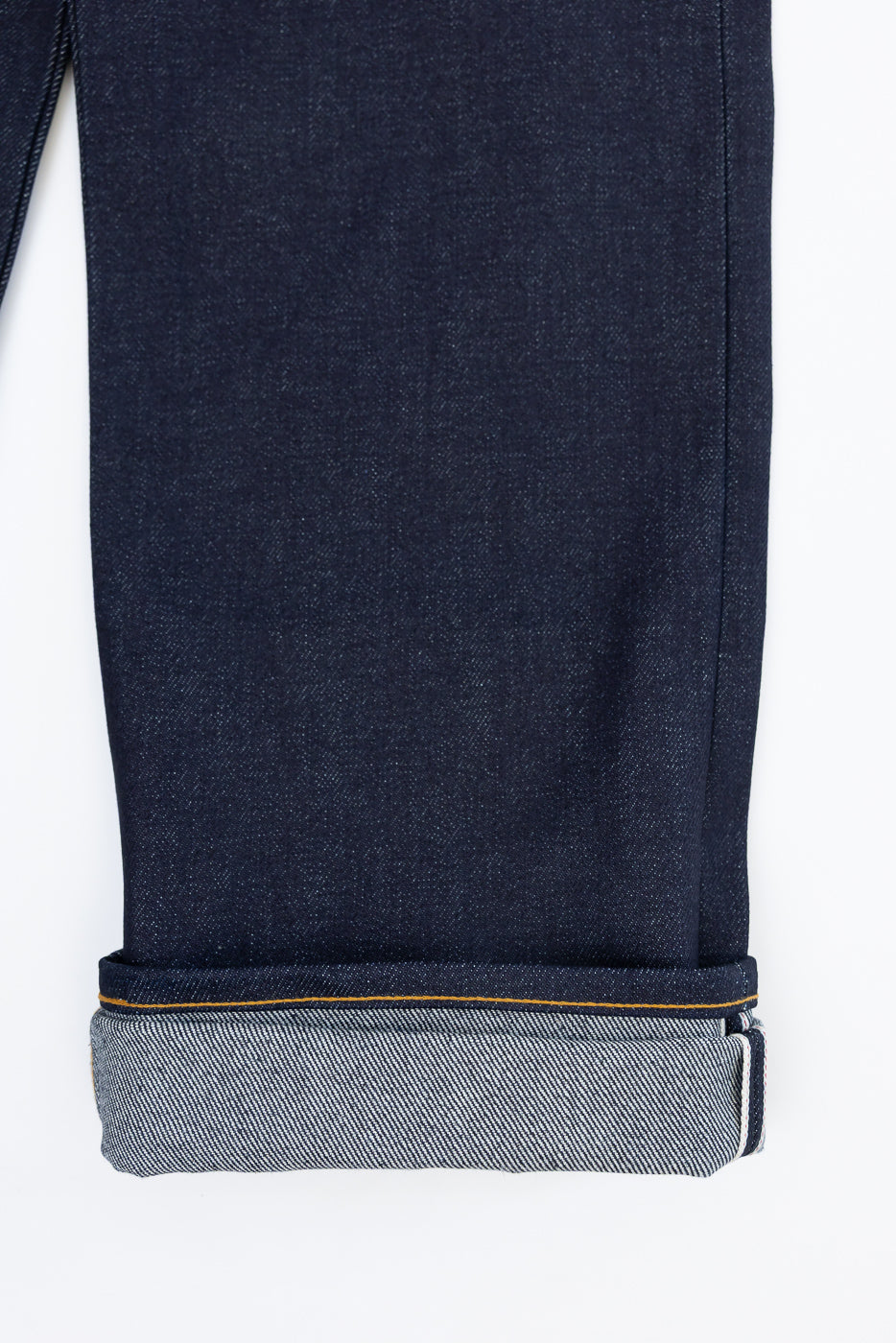 Close-up of the cuffed hem and selvedge detail on the bottom of dark indigo denim jeans.