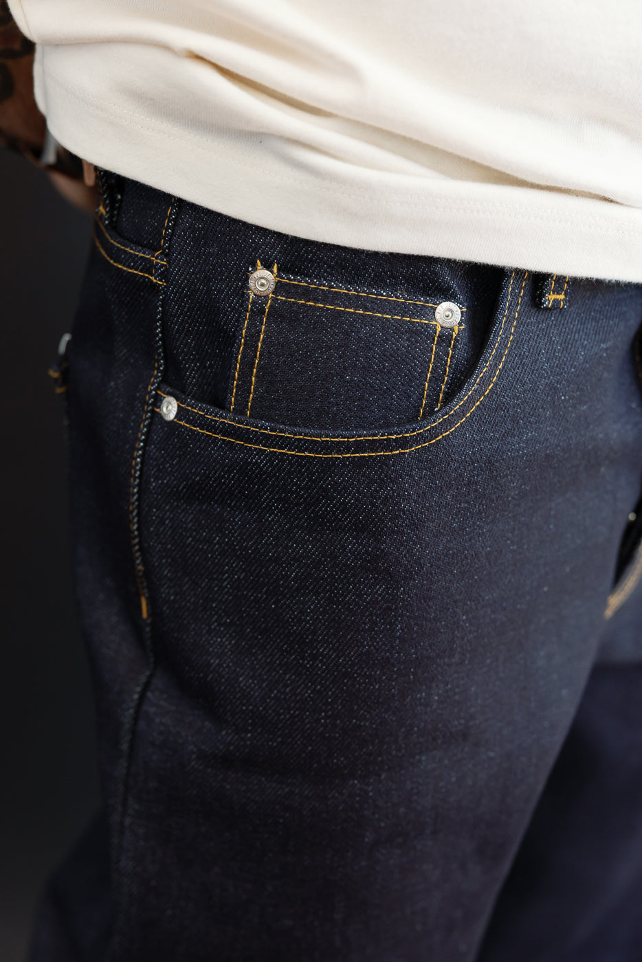 Close-up of the back right pocket of dark indigo selvedge denim jeans on a male model.