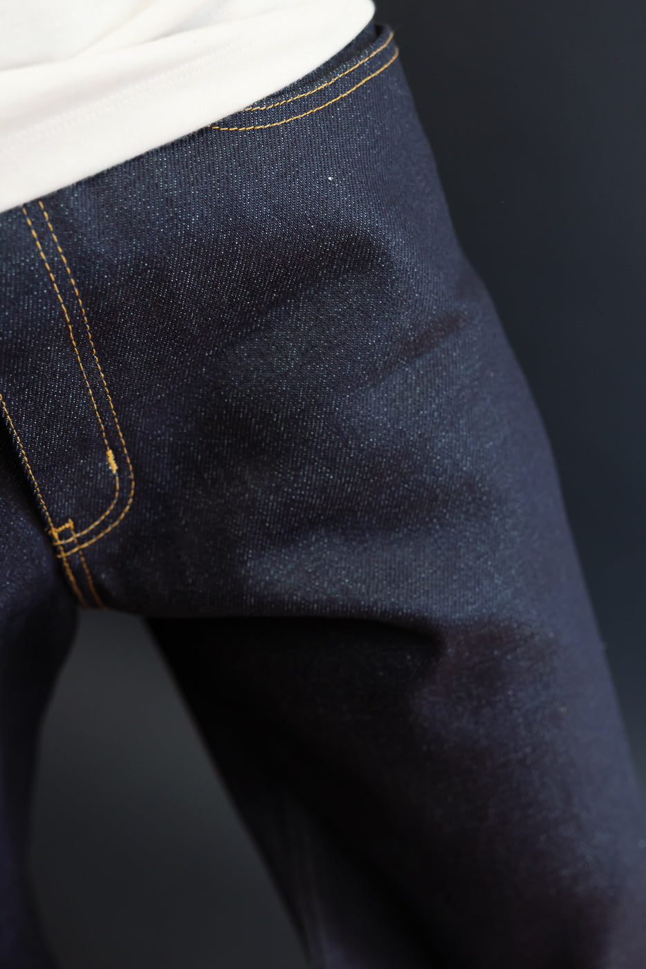 Close-up of the front waistband and hip area of dark blue selvedge denim jeans.