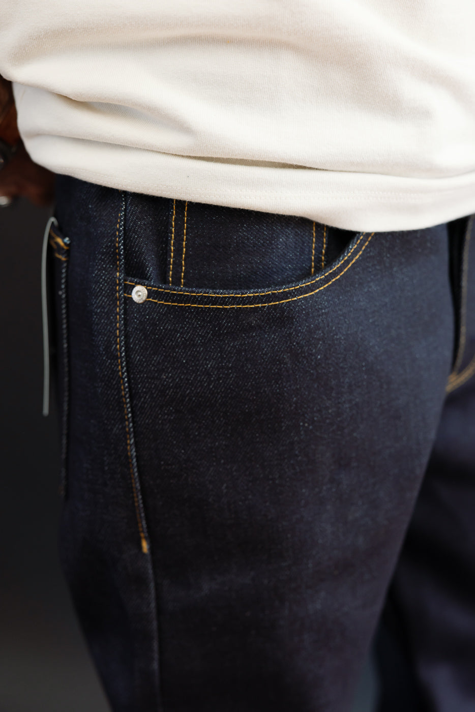 Close-up side view of dark indigo selvedge denim jeans on a male model, showing back pocket detail.