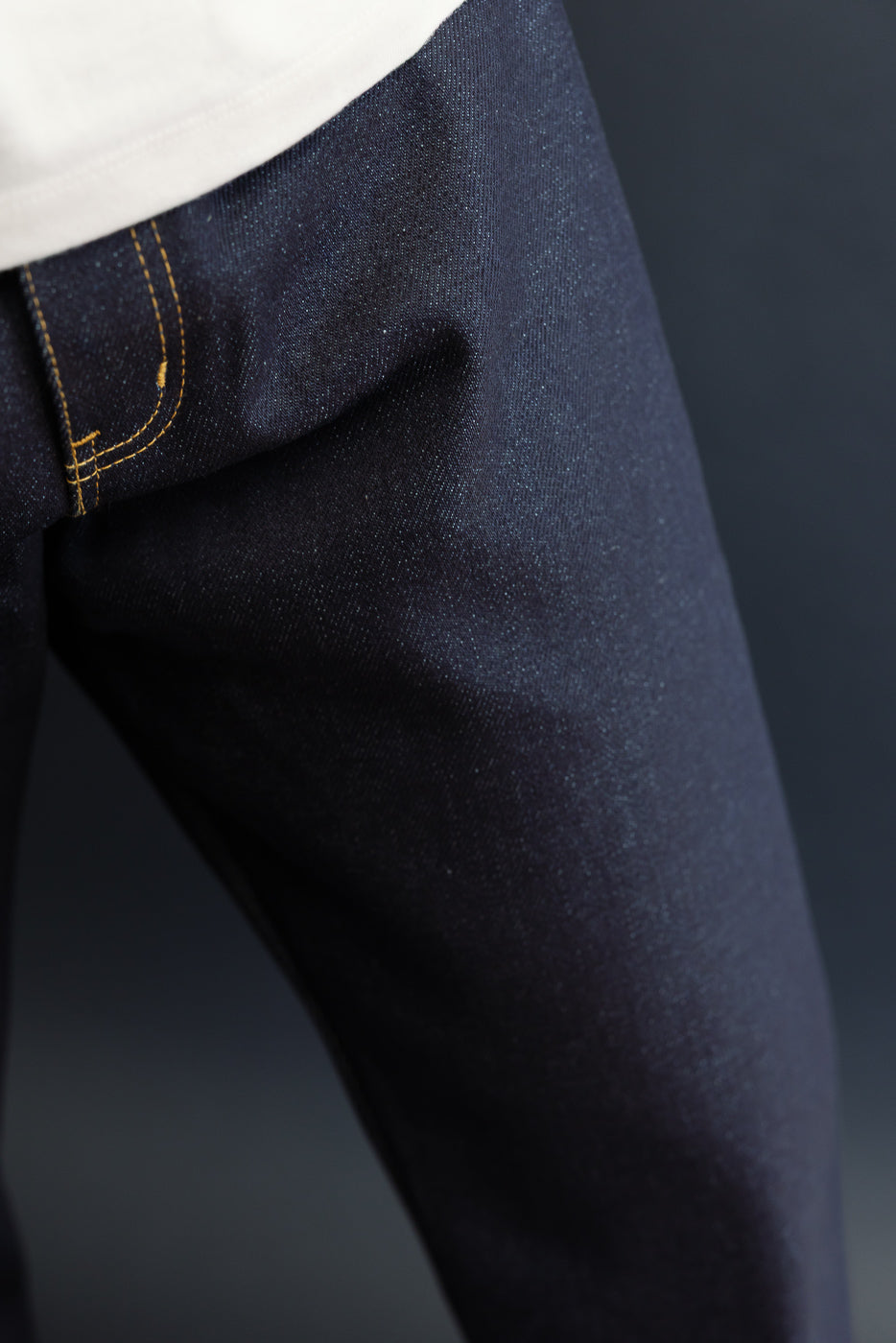 Close-up of the front waistband and dark indigo denim fabric texture on a male model.