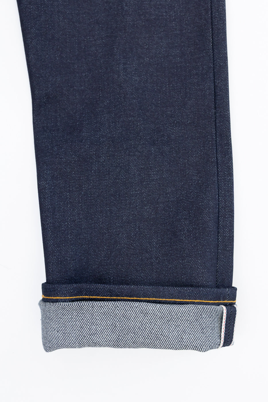 Close-up front view of dark indigo selvedge denim jeans cuff showing white and red edge detail.