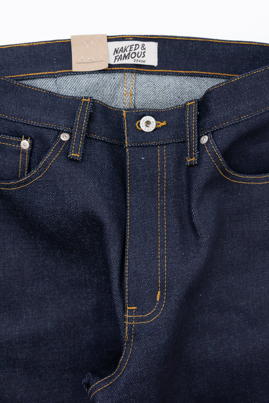 Close-up front view of Naked & Famous Denim jeans showing the waistband, button fly, and tag.