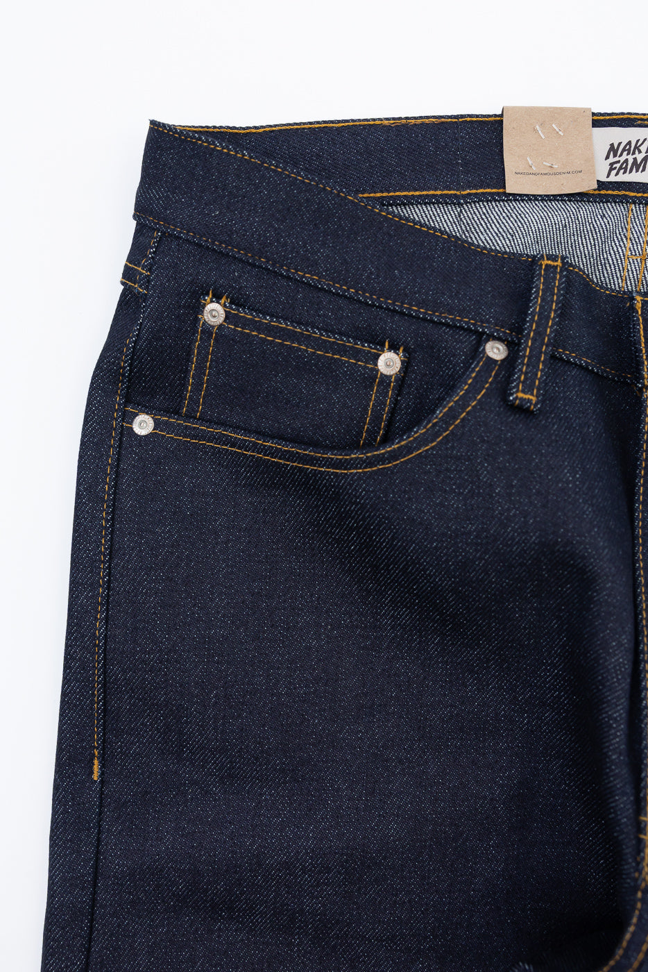 Close-up front view of dark indigo selvedge denim jeans showing waistband and pocket detail.