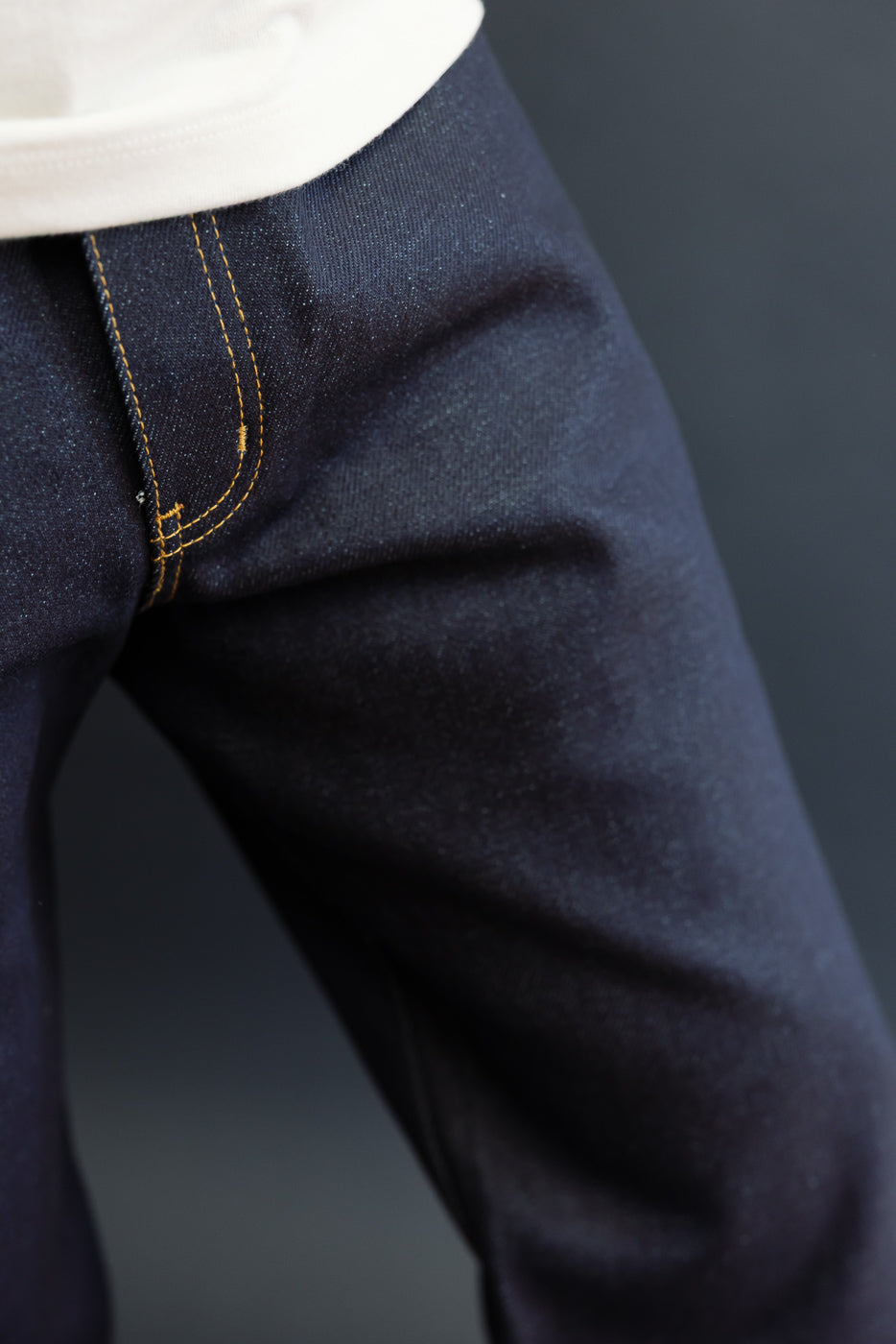 Close-up of the front waistband and fly area of dark blue denim selvedge jeans.