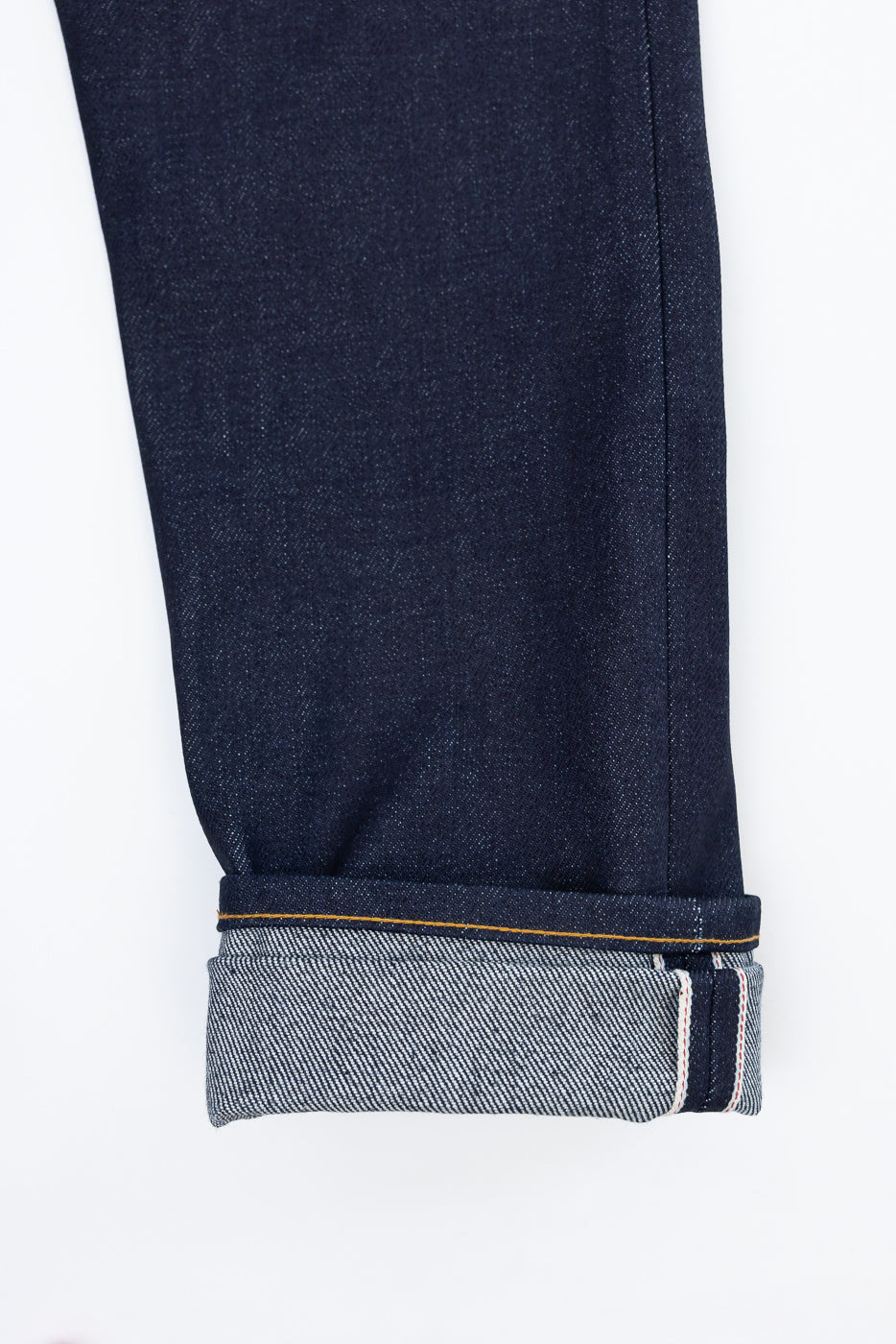 Close-up of the bottom hem and selvedge cuff of the front of dark indigo denim jeans.