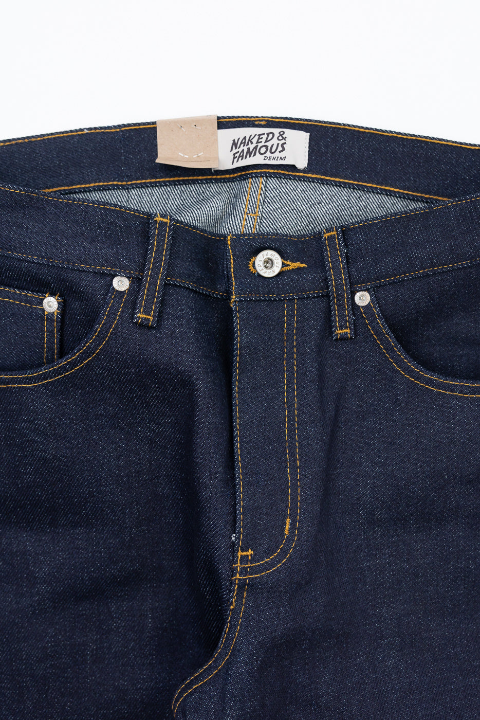 Close-up front view of dark indigo denim jeans showing waistband, button fly, and stitching.