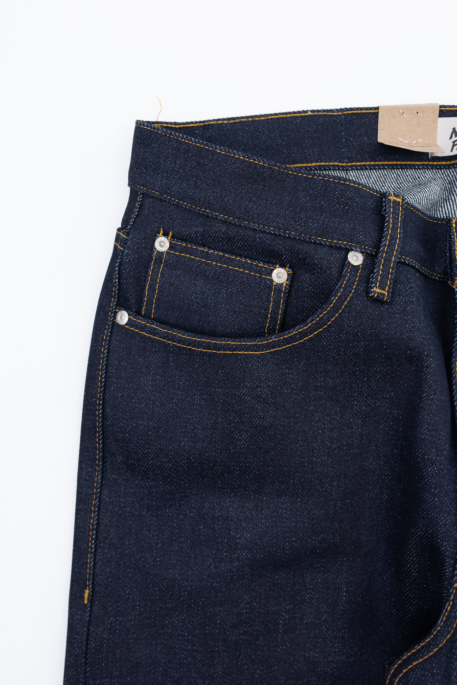 Close-up front view of dark indigo selvedge denim jeans showing pocket stitching and rivets.