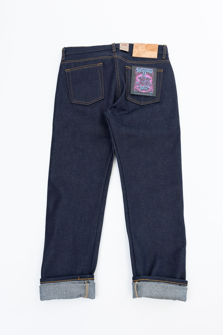 Back view flat lay of dark indigo selvedge denim jeans with cuffed hems and brand tags.
