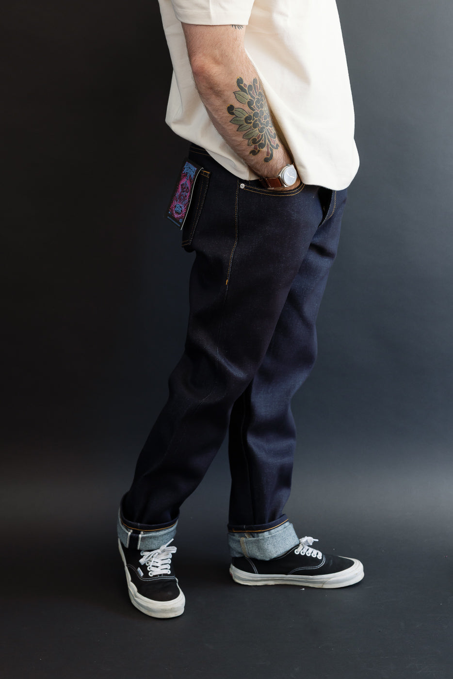 Side view of male model in dark selvedge denim jeans and black sneakers, full body shot.