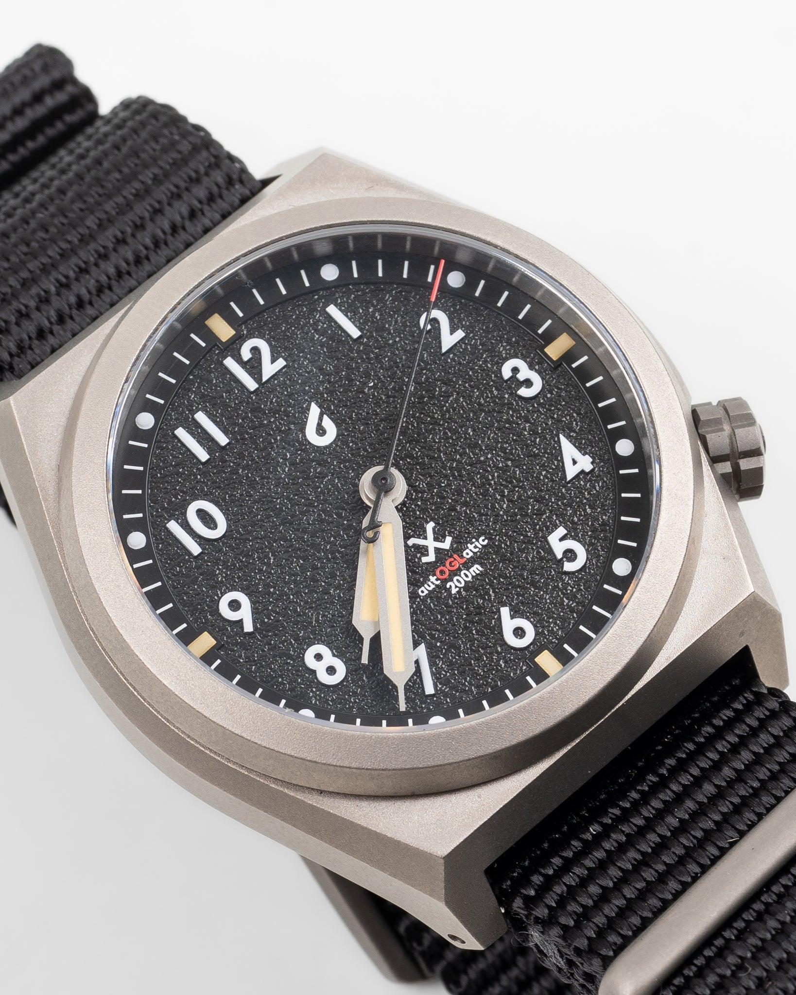 Close-up of black dial automatic field watch, front view, showing dial texture and nylon strap
