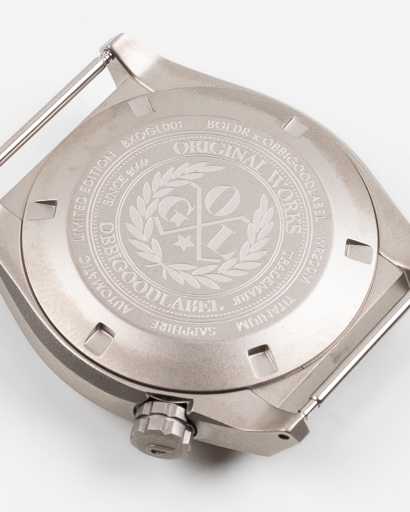 Close-up of engraved titanium watch case back, showing detailed brand markings and crown.