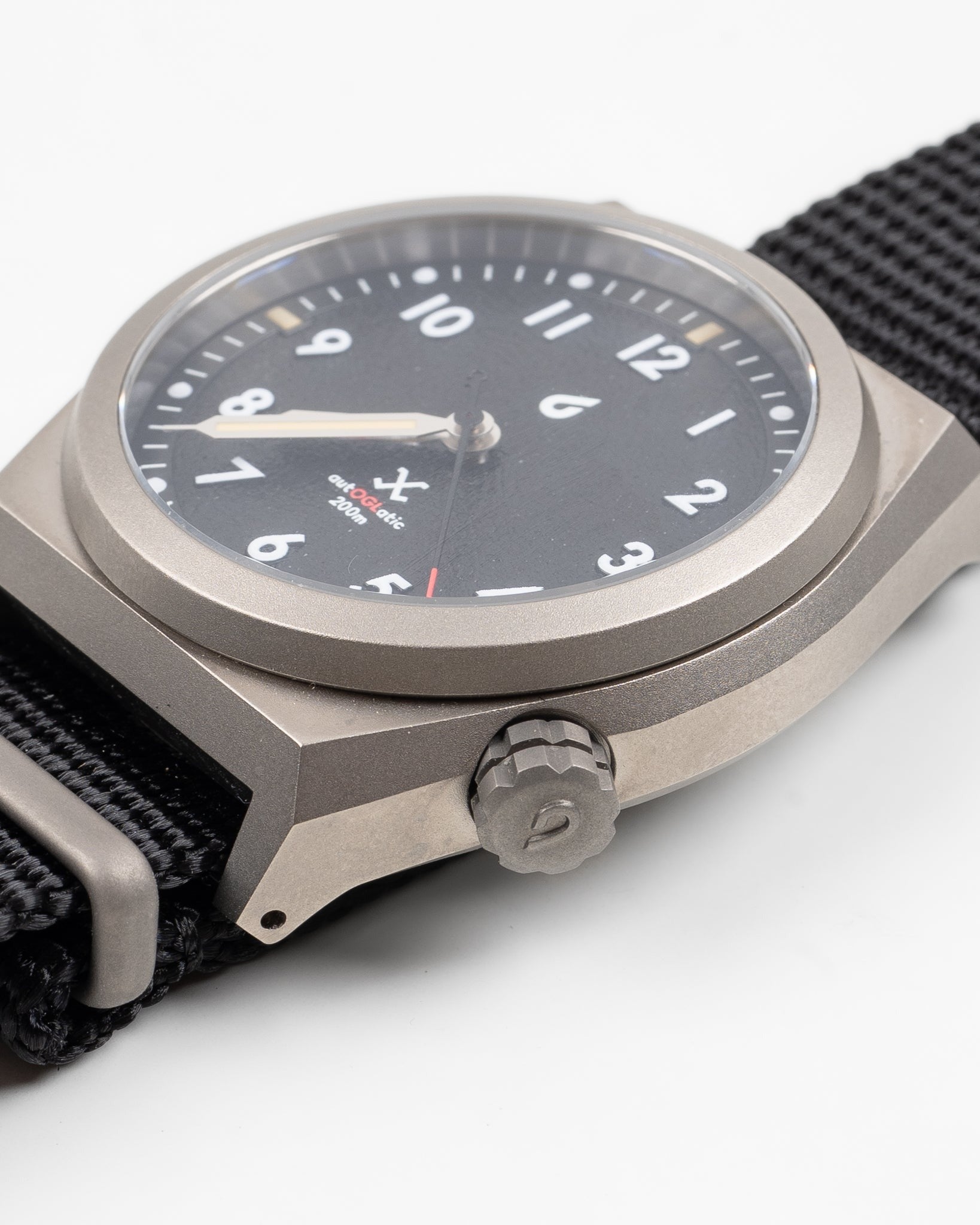 Close-up side view of black dial field watch, showing crown, case edge, and nylon strap details.