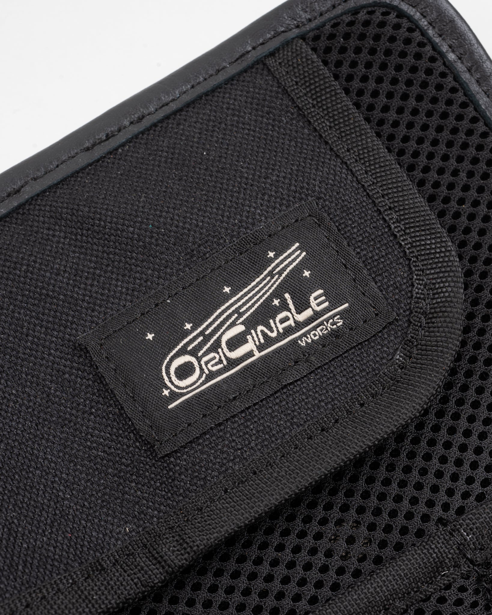 Close-up of black accessory's interior with mesh panel, tag detail, fabric texture, front view