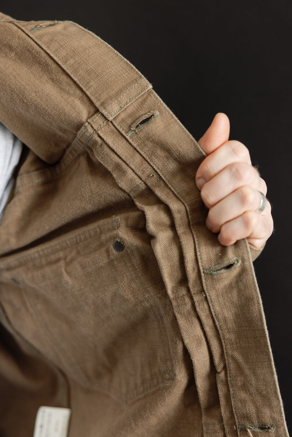 Close-up of the 01507-HOX-BRK jacket's interior, showcasing the brown khaki sulfur-dyed oxford fabric with visible pocket and button-hole stitching, highlighted by the brand's attention to workwear detail.