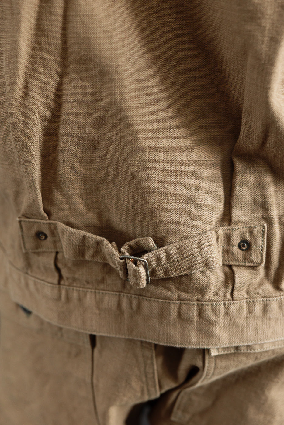 Close-up of the 01507-HOX-BRK - 13oz Brown Khaki Sulfur Dyed Heavy Oxford Jacket - Type I, featuring the textured fabric, back-waist hem detail, and adjustable cinch strap with metal buckle.