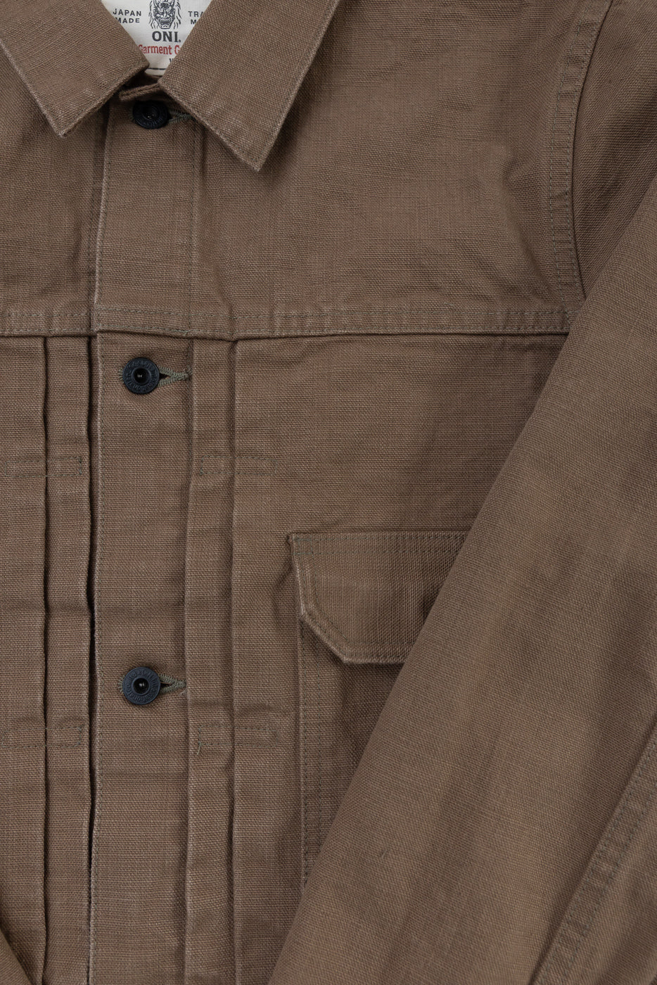 Front view of the 01507-HOX-BRK - 13oz Brown Khaki Sulfur Dyed Heavy Oxford Jacket - Type I, featuring a pointed collar, black buttons, and a chest flap-pocket, highlighting its textured, Japan-made fabric.