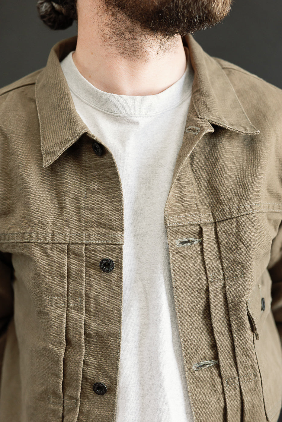 The 01507-HOX-OLB - 13oz Olive Khaki Sulfur Dyed Heavy Oxford Jacket - Type I features an olive-khaki canvas, visible black snap buttons, and an unbuttoned design over a light grey T-shirt.