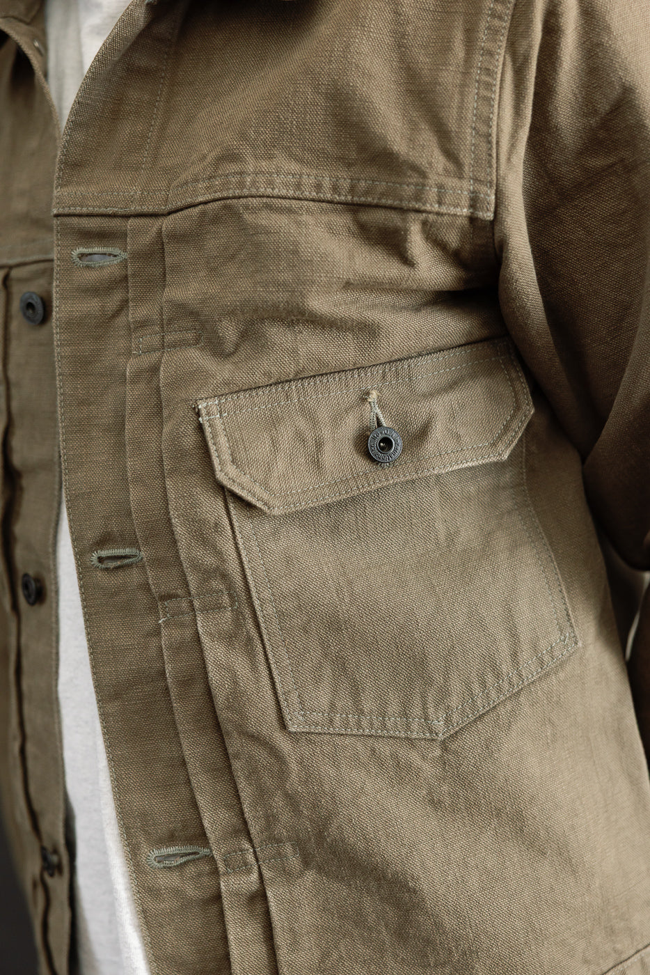 Close-up of the 01507-HOX-OLB - 13oz Olive Khaki Sulfur Dyed Heavy Oxford Jacket, showcasing the buttoned front placket and patch pocket with flap, highlighting its textured, dense fabric and classic workwear silhouette.