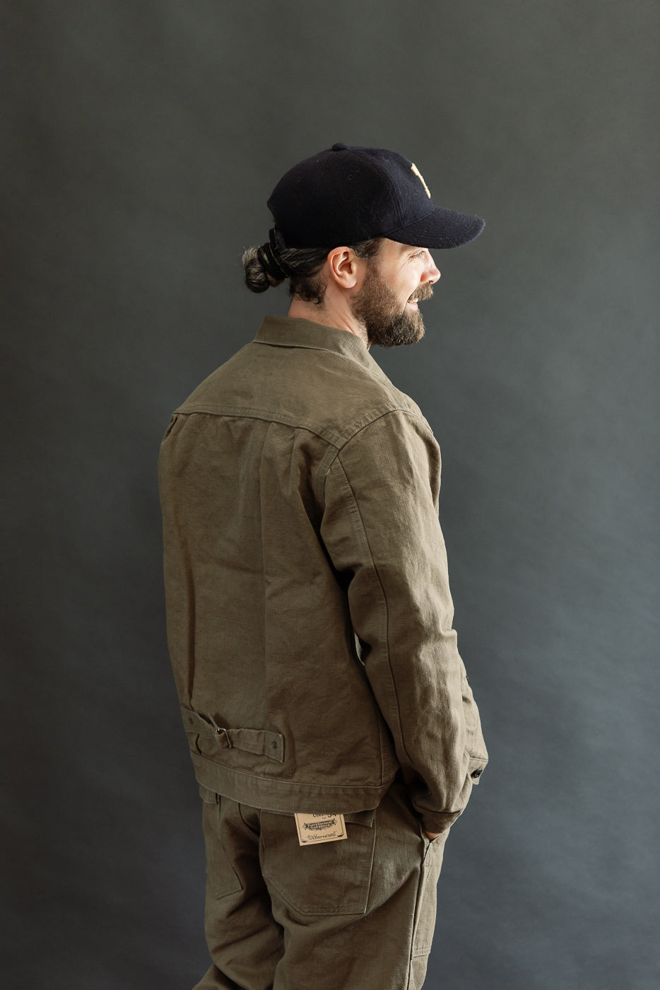 The image features the 01507-HOX-OLB - 13oz Olive Khaki Sulfur Dyed Heavy Oxford Jacket - Type I, showcasing its classic workwear silhouette with pleats, copper rivets, and a cinch back.