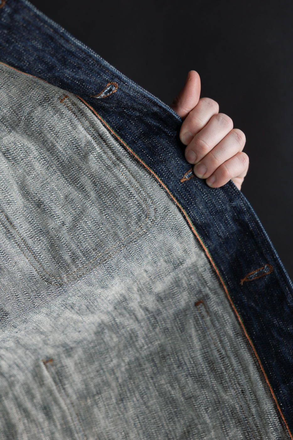 Close-up of the inside selvedge edge and stitching on a denim jacket front panel.