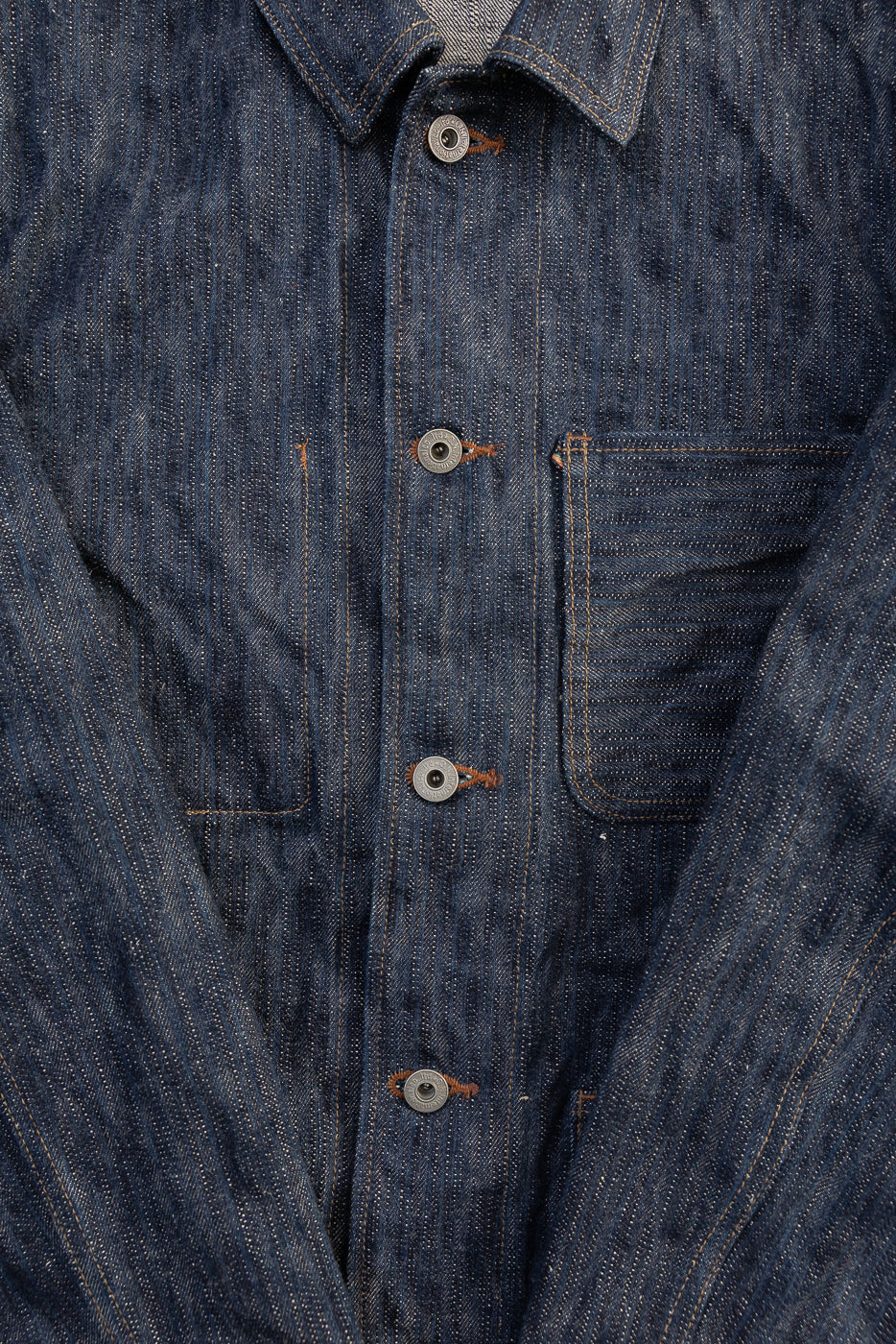 Close-up of front chest and buttons on blue selvedge denim jacket, showing pocket and fabric texture.