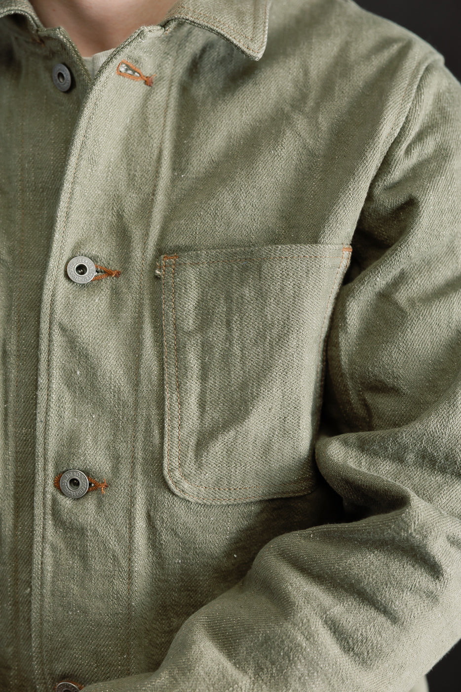 Close-up front view of olive selvedge denim jacket chest pocket, buttons, collar, on male model 5'9